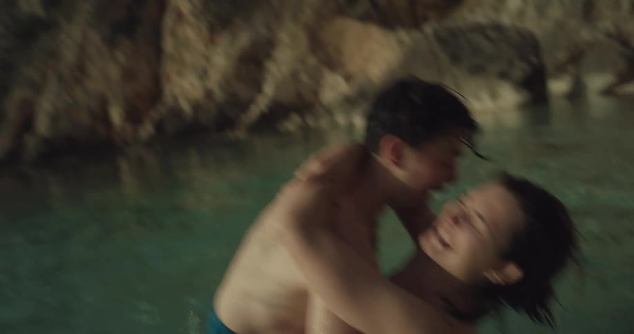 A man and woman in a lake splash one another and laugh and kiss