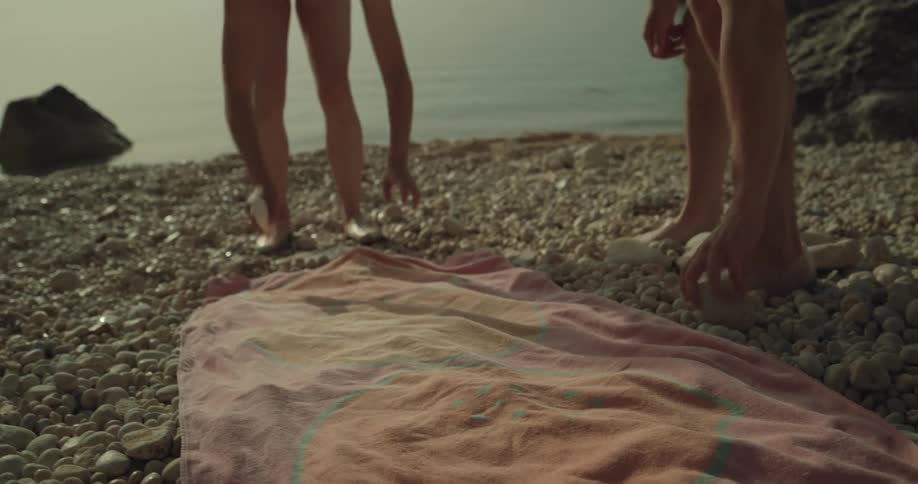 Young woman laying down a towel over the pebbles on a beach