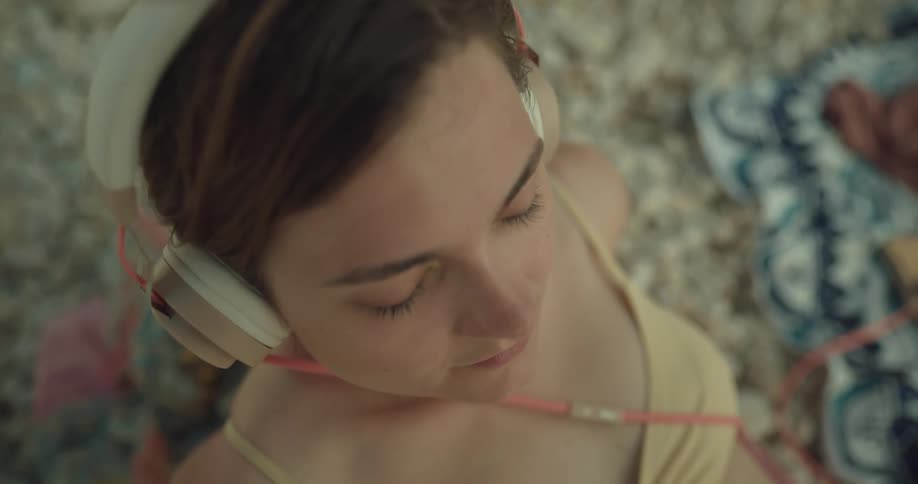 Woman wearing bikini bobs her head while sitting on shore listening to music