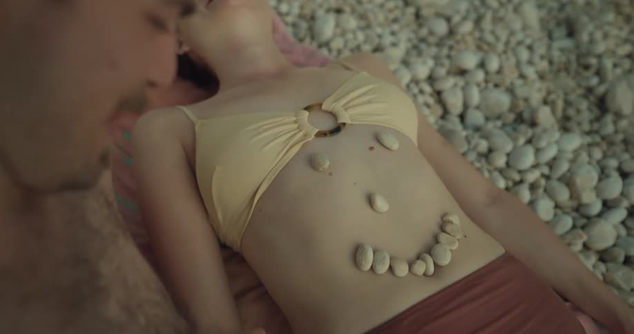 64 5000 eviri sonular man puts pebbles on womans stomach one by one smilingon pebble beach
