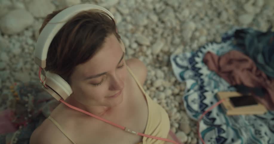 Woman in bikini relaxing on the beach listening music from her phone using headphones