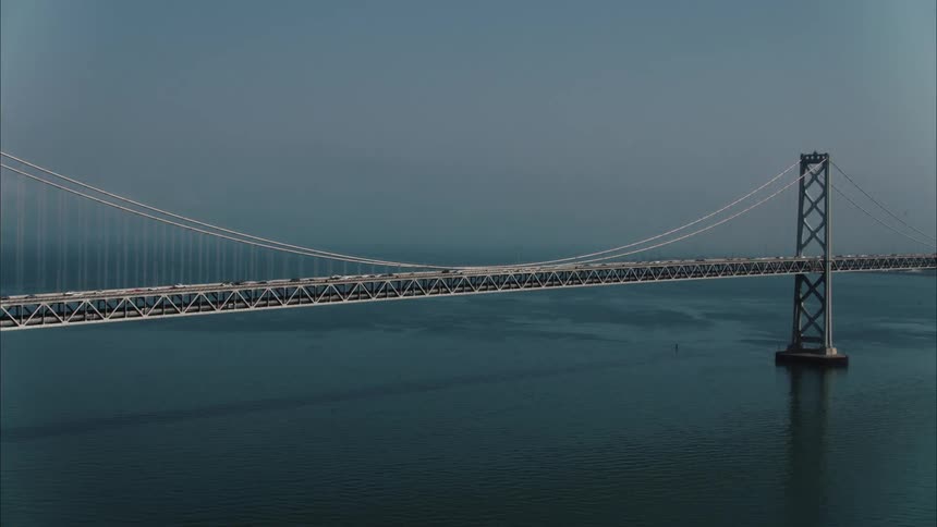 A bridge with vehicles over a body of water with the sky and clouds in the background