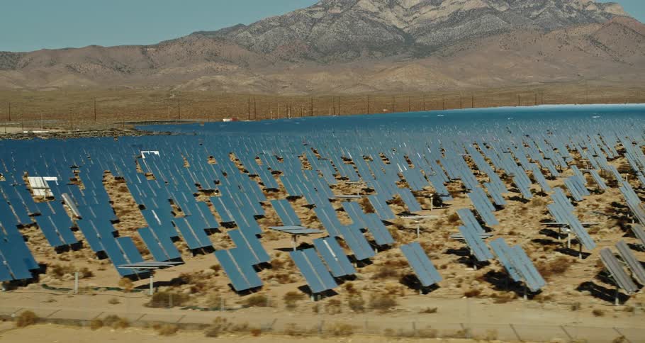 An aerial view of a large array of solar panels in a desert with a mountain in the background