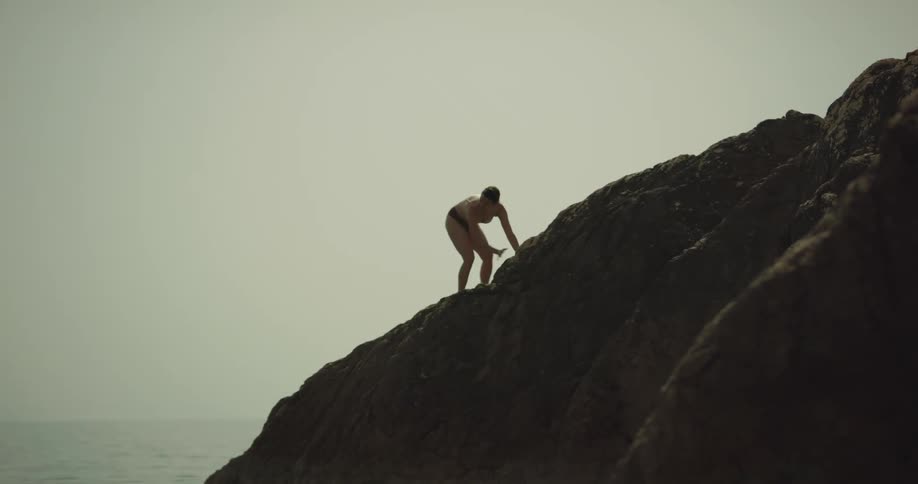 A man claps his hands over his head before jumping off rocks and into the ocean
