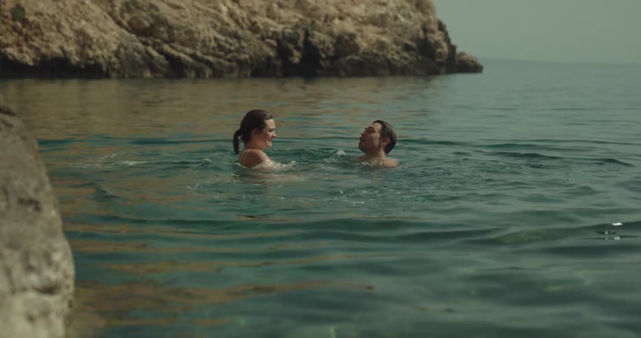 Couple splashes in water near shore sharing a kiss