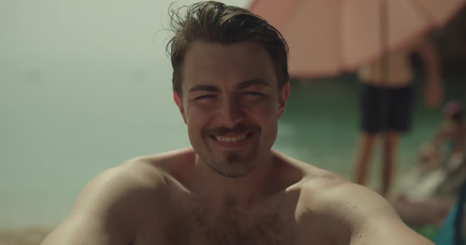 A man sits on the beach and smiles as he runs his hand through his hair