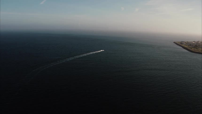 A motor boat is sailing across a lake along the coast