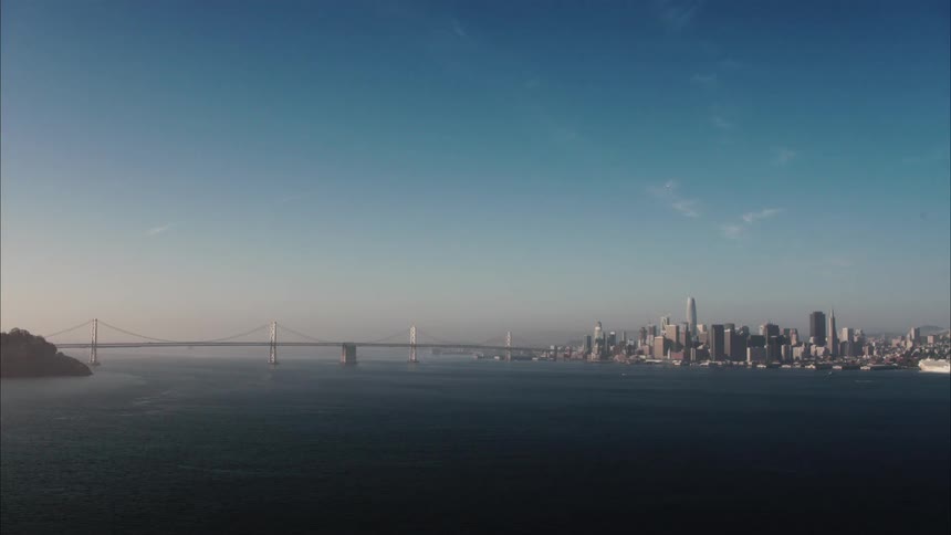 View of a city skyline with high rise buildings and a suspension bridge across the water