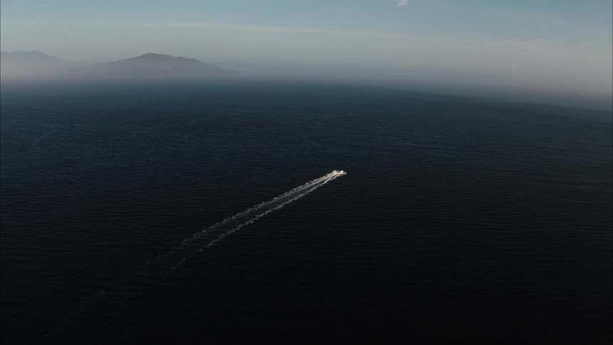 Boat leaves wide wake across dark blue water as fog obscures shore and islands on horizon