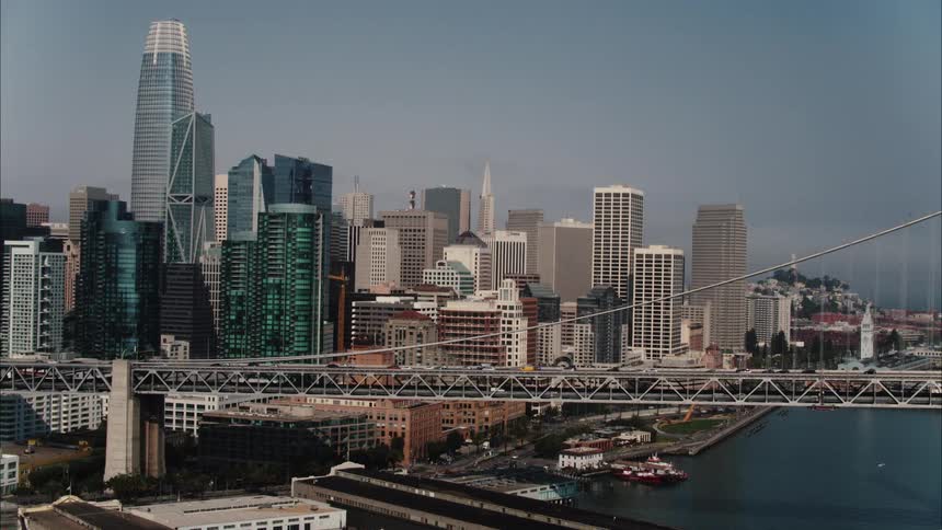 An aerial view of the downtown area of a large city with a suspension bridge and waterway in the daytime