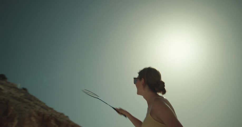 Young woman wearing bikini playing badminton on a beach near a cliff