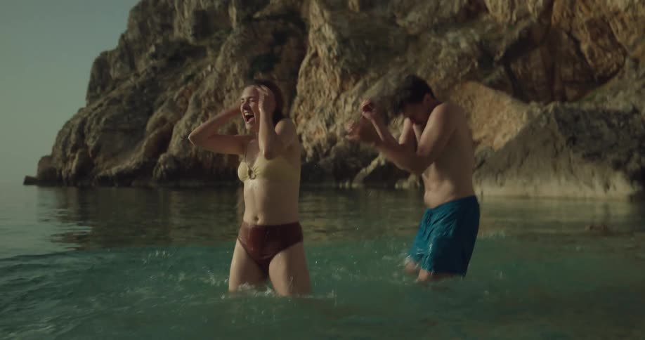 A man and woman run into the ocean water and start playing splashing each other