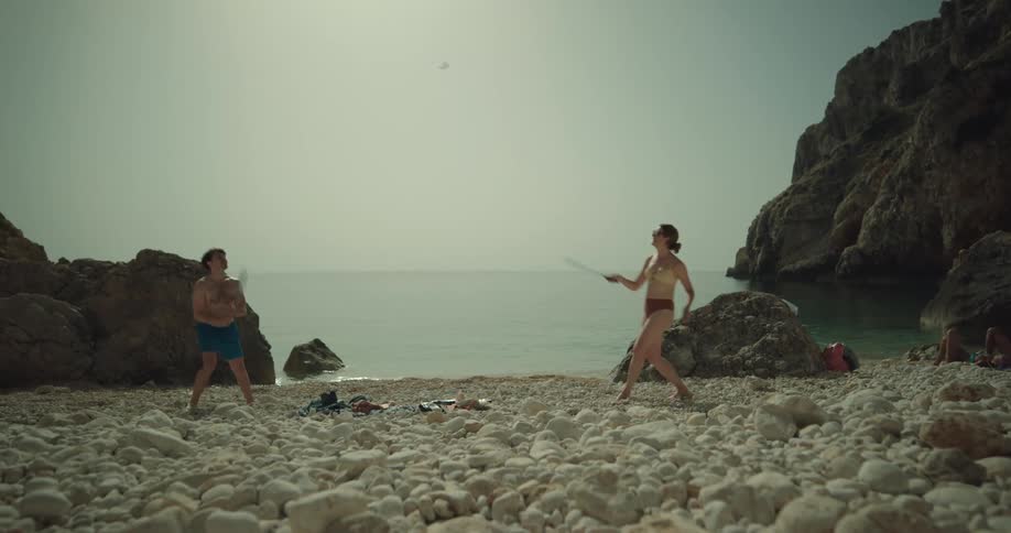 A man and a woman are playing badminton on a beach and dressed in swimming clothes