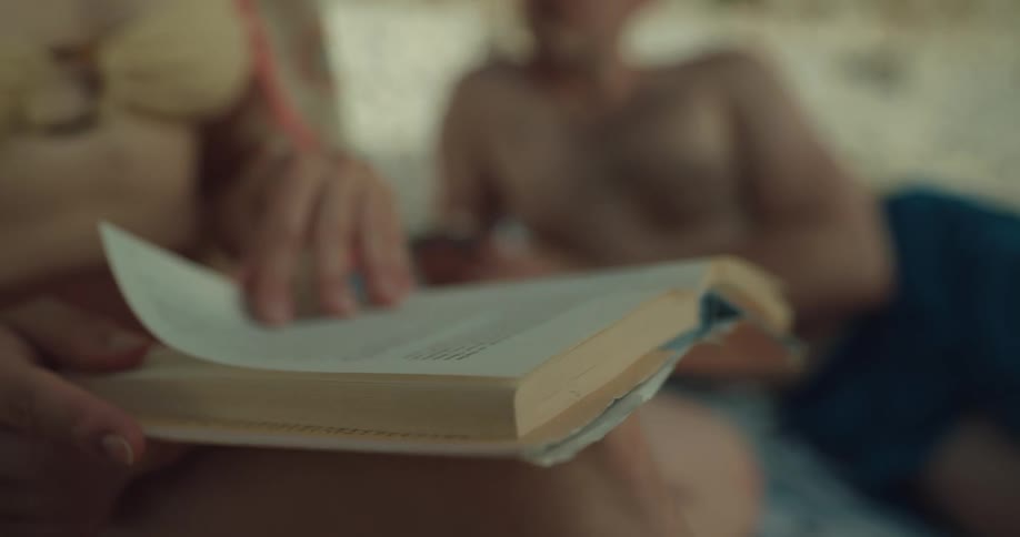 Woman sitting over a towel on the beach reading a book next to a man
