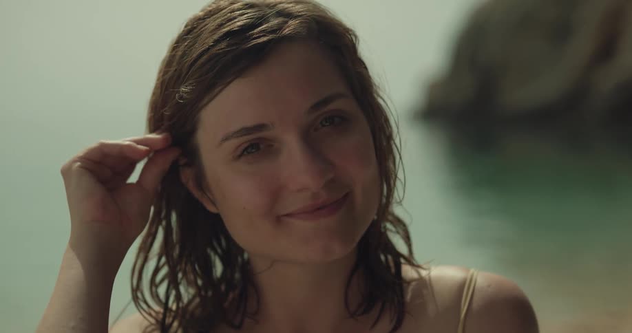 A woman on the shore smiles as she brushes her hair behind her ear