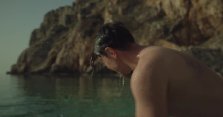 Man and woman splash water on each other in sea at pebble beach
