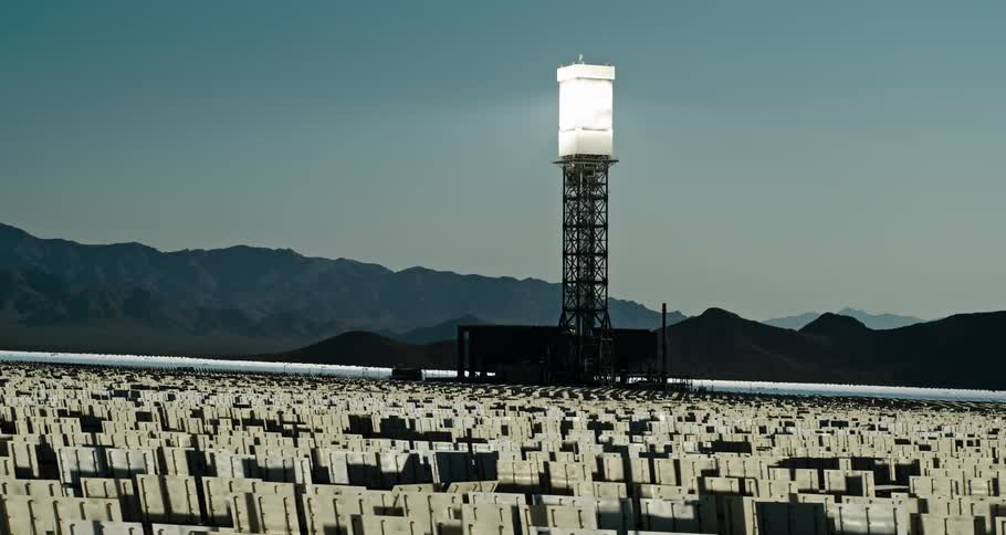 A landscape with solar reflectors with a mountain range the sky and clouds in the background