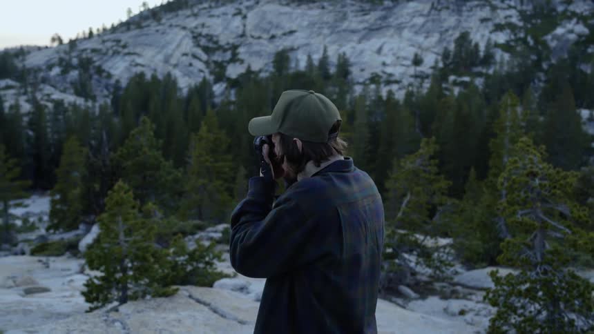 A man is taking photographs on a mountain covered with trees