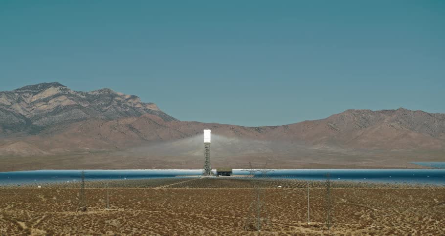 Antennas and a light tower sit in a desert near a lake and canyon