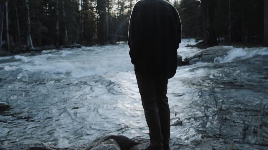 A man stands on some rocks near a rough stream