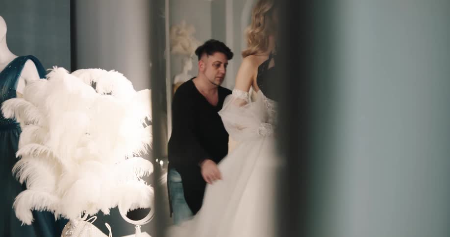 A woman in a wedding dress smiles as another woman touches her makeup up and a man adjusts her dress