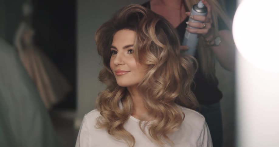 Hair stylist uses hairspray on a client sitting in front of the mirror