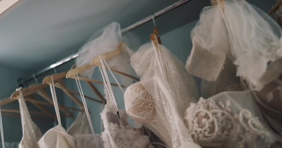 White lace decorated wedding dresses hang on pole in shop