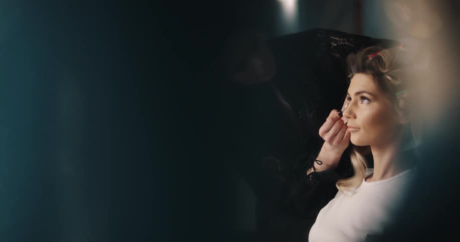 A makeup artist in a boutique is applying makeup to a woman with rollers in her hair