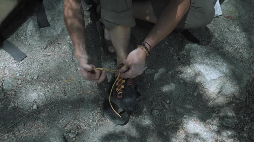 Man sits next to a tent, tying his shoe