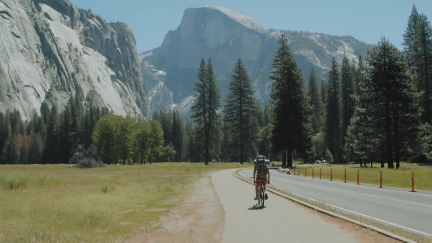 A man rides his bike down a bike path near a mountain