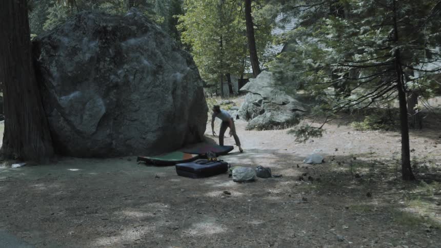 A man is setting up camp by a boulder
