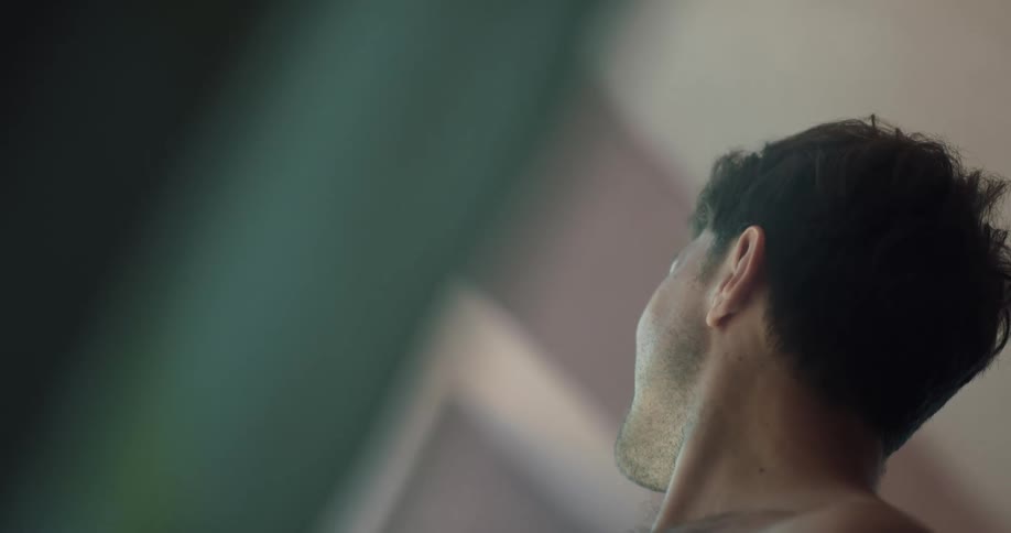 A man brushes his hair back by the window