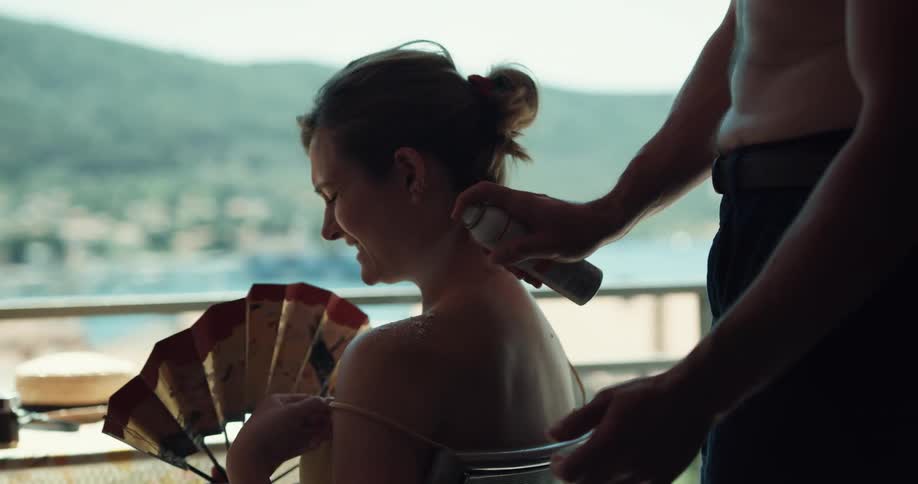 A man sprays suntan lotion on a womans back