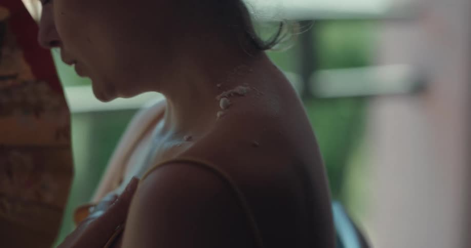 Man sprays and carefully spreads treatment onto womans sunburned back and neck as she fans herself