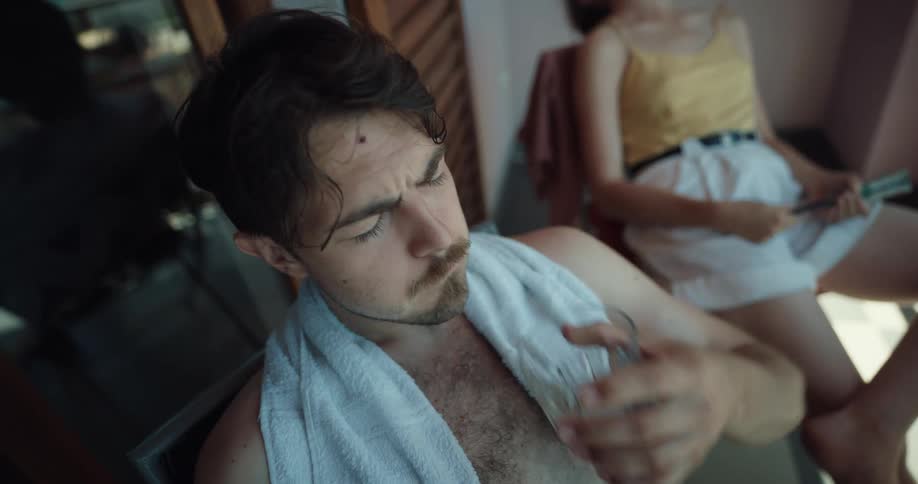 Man and woman sit on balcony on hot day drinking water and fanning themselves