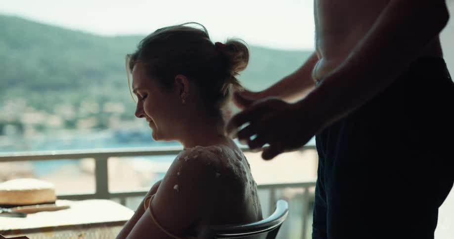 Shirtless man puts on sun cream on womans shoulder using hand fan