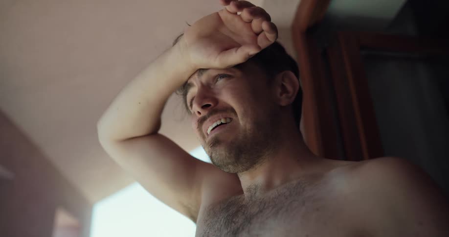 A bare chested man is looking around and rubs his hand across his forehead