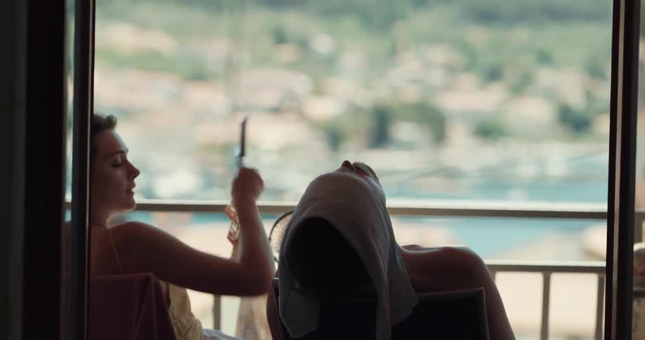Shirtless man puts wet towel on his head while woman uses hand fan on the balcony getting exhausted from heat