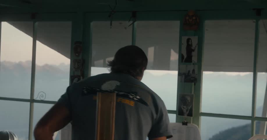 Man drinking from a cup looks at the mountains through the windows of a cabin
