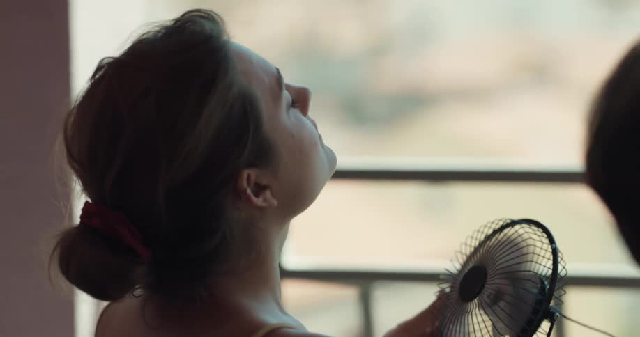 A woman in a man on a balcony with the woman holding a small electrical fan