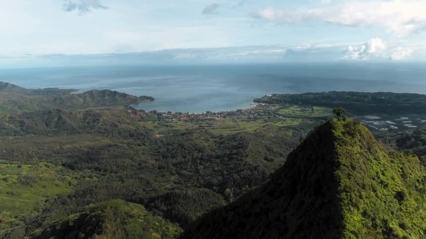 Drone shot flying over mountain ridge toward tropical kauai bay