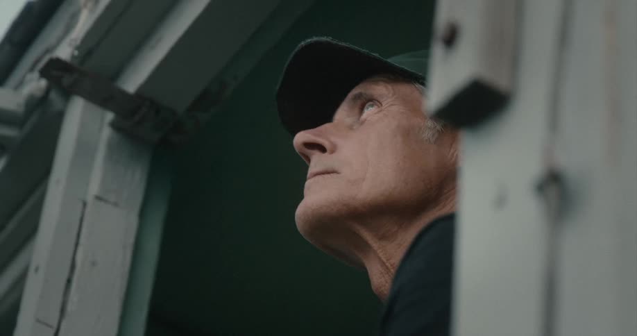 Man wearing a green baseball cap looking out a window