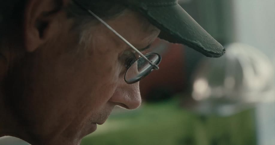 An older man wearing glasses is indoors and looking downwards
