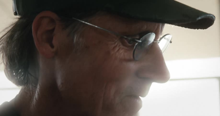 Bright sunlight comes through a window where a man stands inside in a baseball cap
