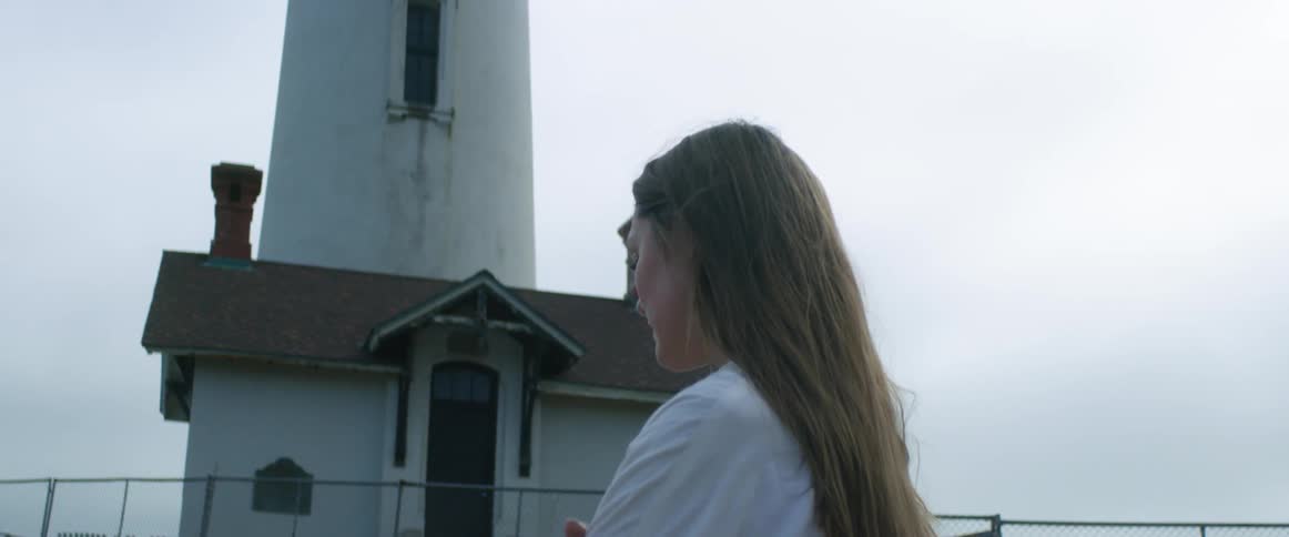 Young woman wearing white shirt standing next to a lighthouse