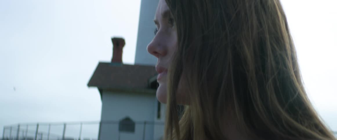 Young woman writing on a tablet near a lighthouse close to the ocean