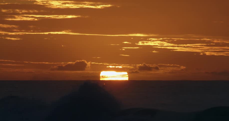 Sun setting behind the clouds in the sky over the ocean waves at sunset