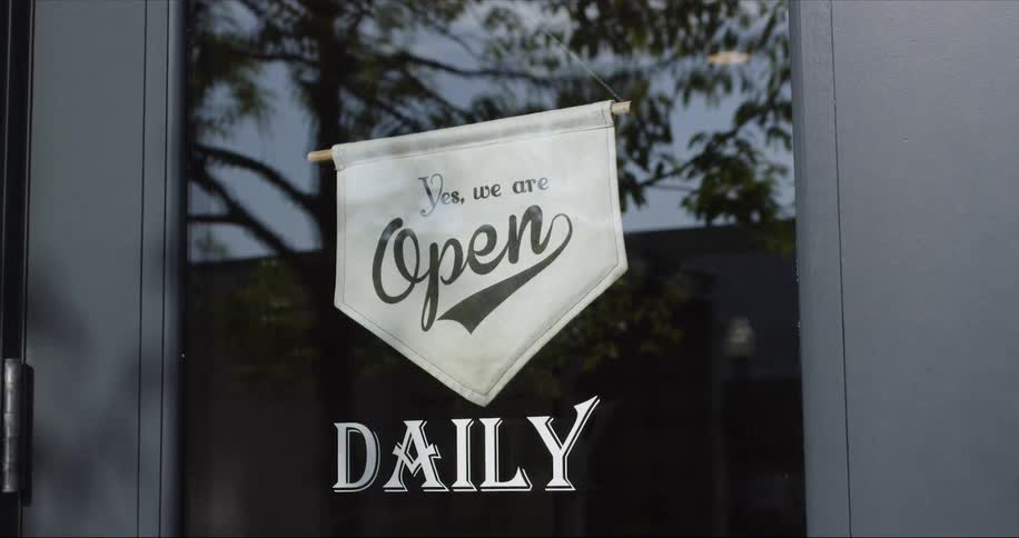 A man walks behind a door in s tore with an open sign on it