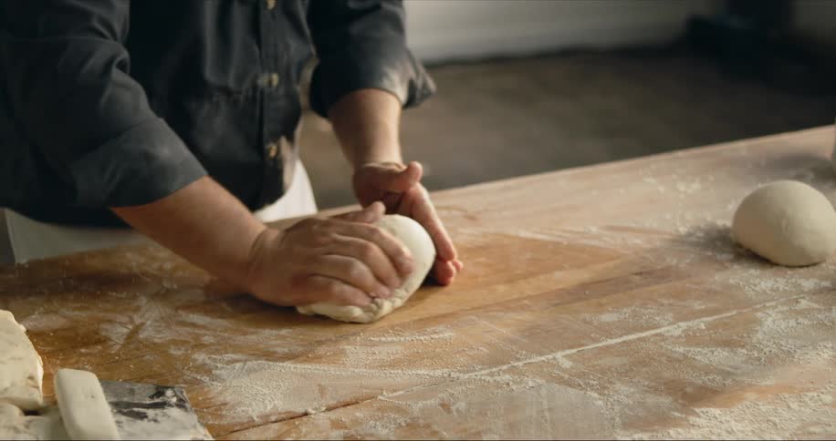 A man rolls a large ball of dough on a floured table top