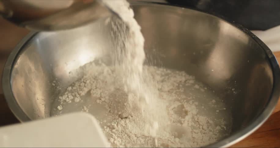 Someone is pouring powder into a silver mixing bowl with some water in it